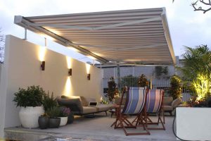 Outdoor living with indoor plants, sofas and resting wooden chairs and red/white striped shades in the night view