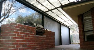 A large backyard area with white shade at the top & beside and backyard grill gas